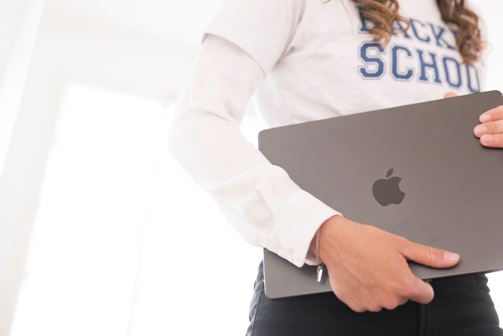Person im Hacker-School-Sweatshirt trägt einen zugeklappten Laptop unter dem Arm