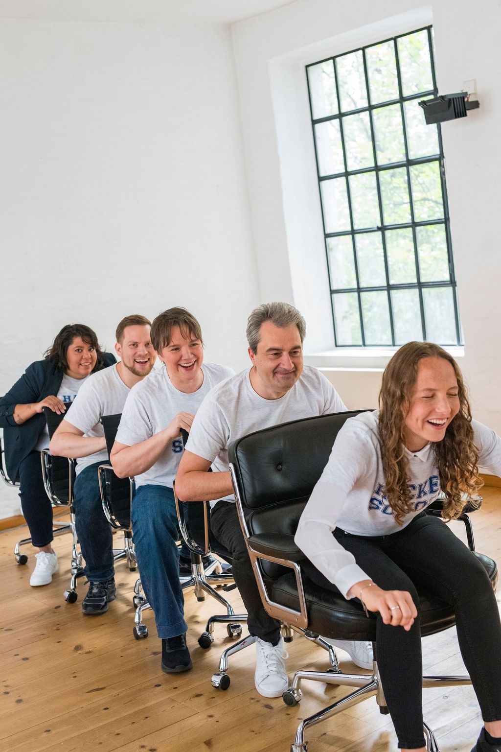 The five founders sitting one behind the other on office chairs in a bright room, laughing