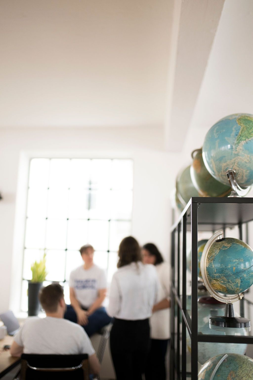 Globes on a shelf in the foreground, with colleagues talking out of focus behind them
